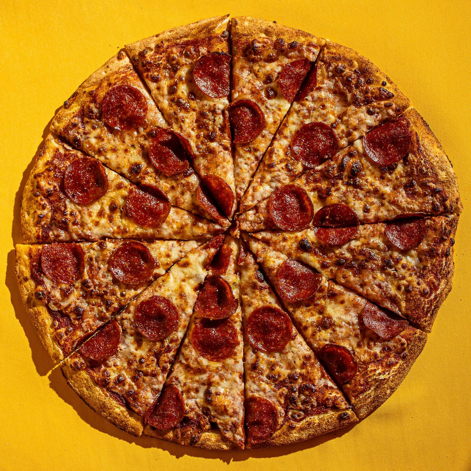 Sliced pepperoni pizza on a bright yellow surface, perfect for food-themed designs.